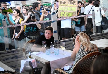 Travelers in Barcelona are targeted by protesters who throw objects and spray water while shouting for them to leave the city.